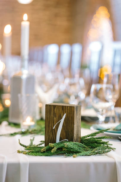 istock nature, catering, dining hall concept. small dark wooden cube with white number one on the front part of it, it is placed on the table for marking and surrounded with small conifer branches 886014932