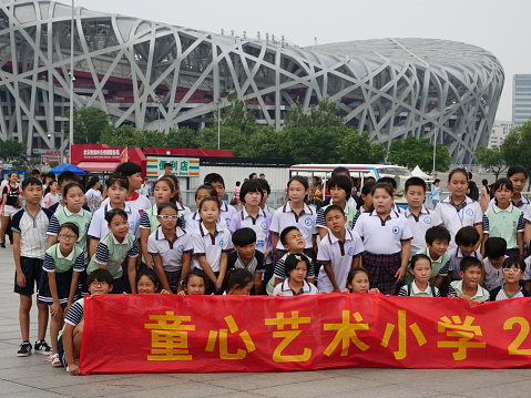 School group smiling for a picture in front of the most represetantive building in the modern Olympia Park in Beijing, the National Stadium, a beloved touristic point specially for Chinese people