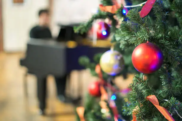 Photo of atmosphere of feast, christmas, music concept. bright multicoloured twinkle lights are reflecting into balls of bright red and golden coloures on the background of piano