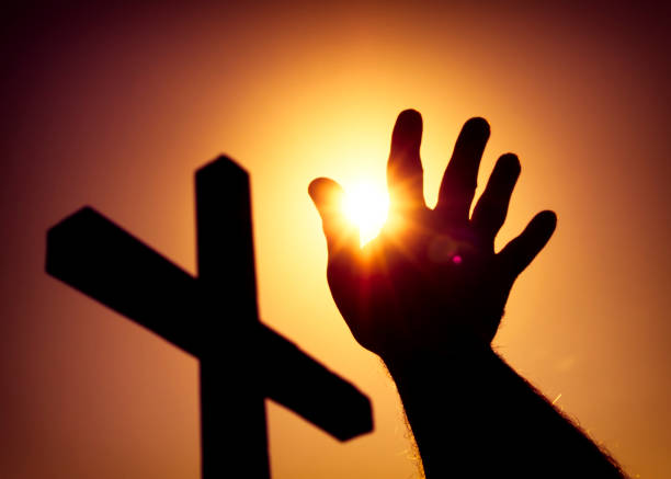istock Silhouetted cross and man's hand with sun 886045712