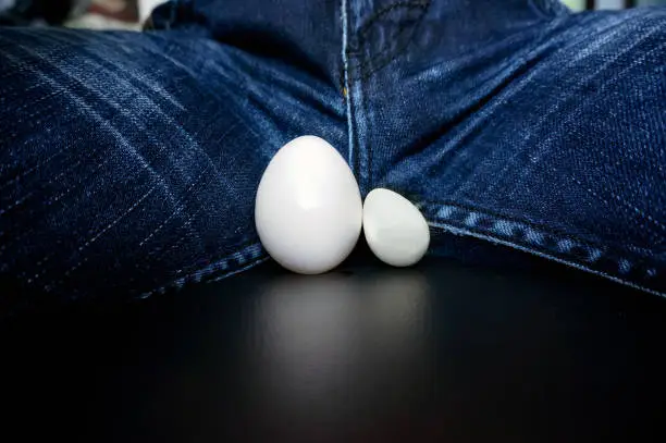 The male testicles, in the form of chicken eggs, between the legs of the guy in the jeans. Disease of male genital organs. inflamed testicles enlarged. testicular cancer
