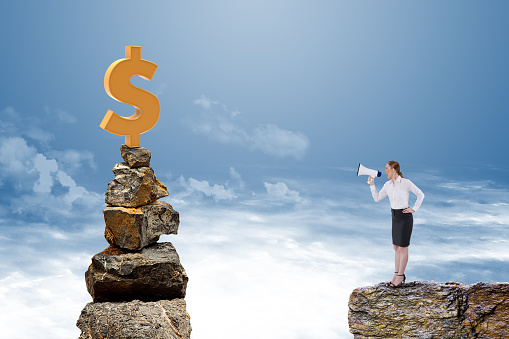 Businesswoman speaking on megaphone with dollar sign on stack of rocks