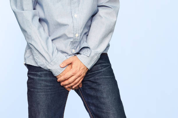 Close up of a man with hands holding his crotch Close up of a man with hands holding his crotch on a light blue background. Urinary incontinence. Men's health. The pain from the blow in groin. sperm stock pictures, royalty-free photos & images