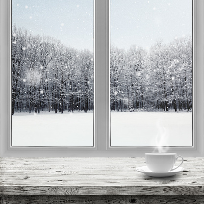 Hot drink in cup on table over winter forest background through window view