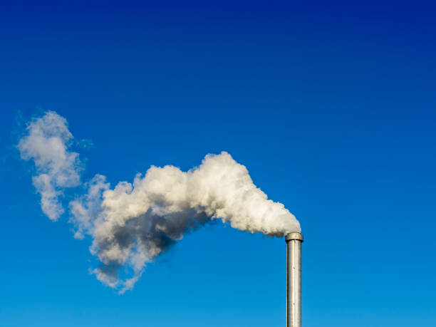 a metallic chimney giving off a heavy cloud of white smoke against a deep blue sky - energia reativa imagens e fotografias de stock