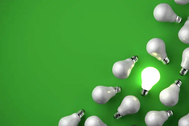 Bright Idea- Standing out of the crowd concept.  One illuminated light glowing while the other bulbs are dark on a green background with copy space.