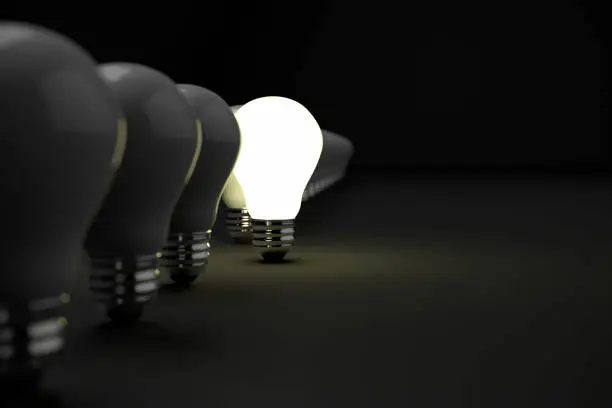 Bright Idea- Standing out of the crowd concept.  One illuminated light glowing while the other bulbs are dark on a black background with copy space.