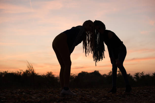 Silhouette of two young women with African braids leaning