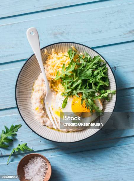 Savoury Oatmeal With Fried Egg Arugula And Cheese Delicious Healthy Breakfast Or Lunch On Blue Wooden Background Top View Stock Photo - Download Image Now
