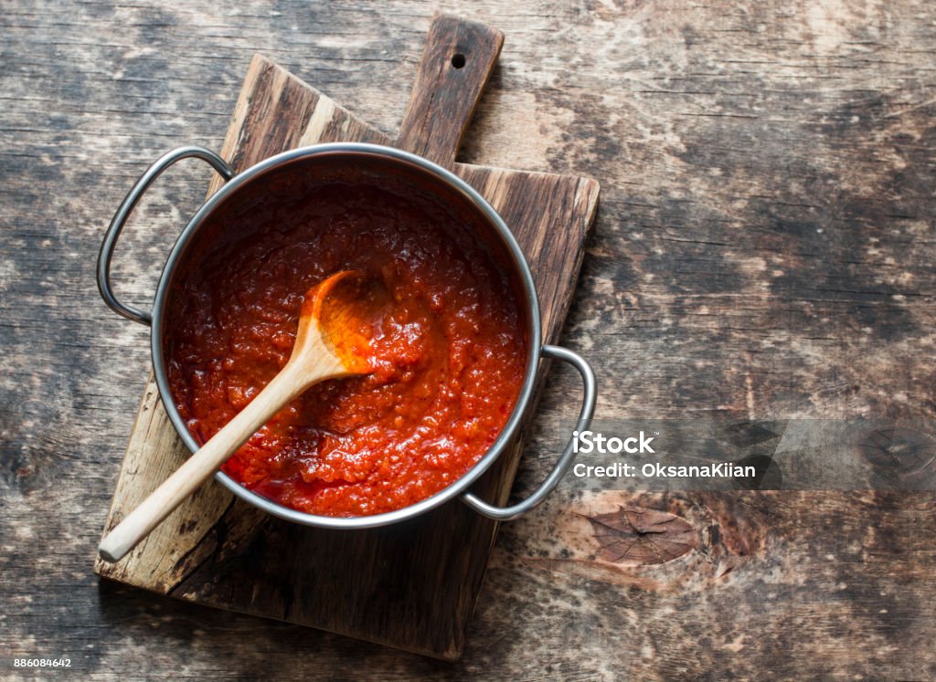 Classic homemade tomato sauce in the pan on a wooden chopping board on brown background, top view. Pasta, pizza tomato sauce. Vegetarian food Tomato Sauce Stock Photo