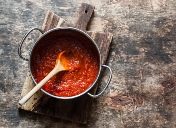 Photo of Classic homemade tomato sauce in the pan on a wooden chopping board on brown background, top view. Pasta, pizza tomato sauce. Vegetarian food