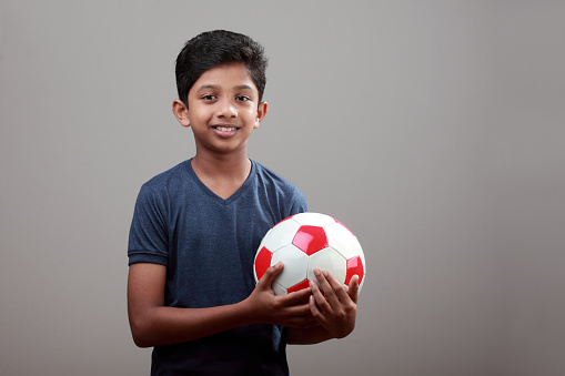 Cheerful young boy holds a soccer ball in his hand