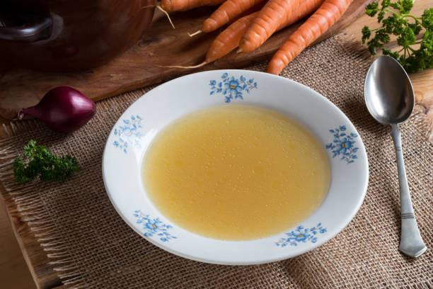 istock Chicken bone broth in a plate, with vegetables in the background 886114974