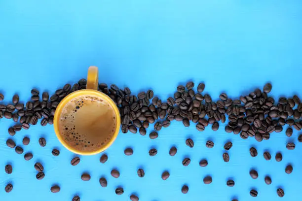 flat layout with a yellow mug of frothy espresso on a blue table with roasted grains
