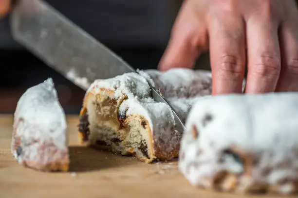 Closeup Female Hands Cutting Mini Marzipan Stollen with Knife on Wooden Board.