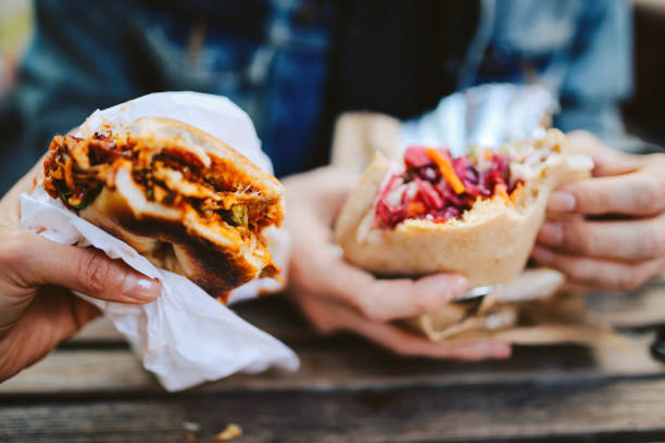 Close up of a Texas pulled pork bbq burger and a falafel outdoors Close up image of two people eating a Texas style pulled pork barbeque and a falafel fast food in East London. street food stock pictures, royalty-free photos & images