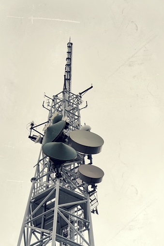 Low-angle vintage shot transmitters and aerials on telecommunication tower with dramatic cloudy sky, digital communicationa and encryption safety concept
