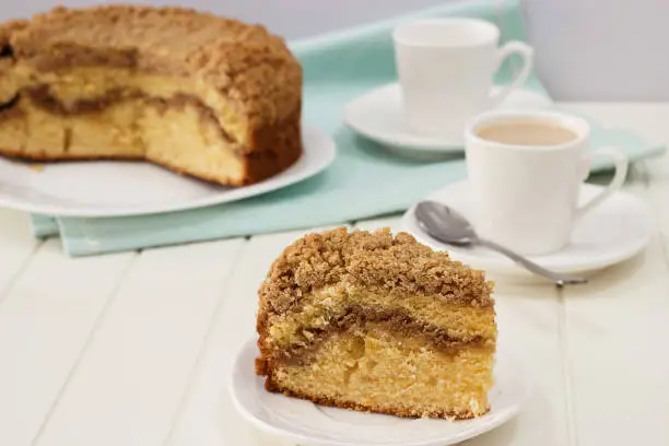 Photo of Close-up piece of homemade Cinnamon crumble coffee cake and cup of milk tea. White wooden background.