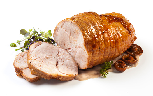 Roasted pork with sauce and garnish isolated on white.
