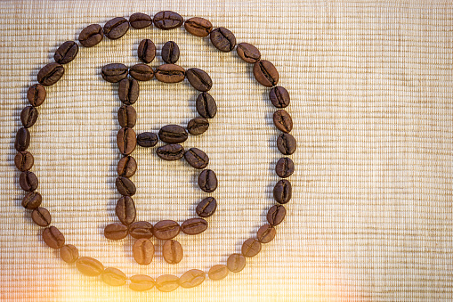 Coffee beans are laid out in the form of a bitcoin sign on a beige napkin. Symbol of growth, progress, recovery, financial well-being.