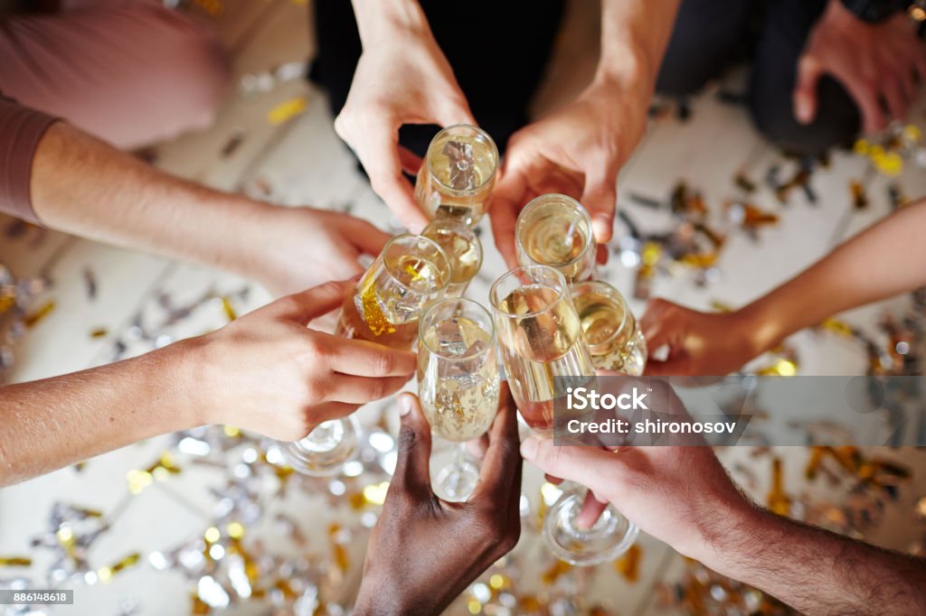 Toasting Several flutes with sparkling champagne in hands of intercultural friends during toast Champagne Stock Photo