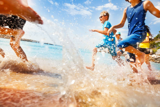 Kids having fun run make splashes in shallow water Group of kids running in shallow sea water making splashes in summer sunny day beach play stock pictures, royalty-free photos & images