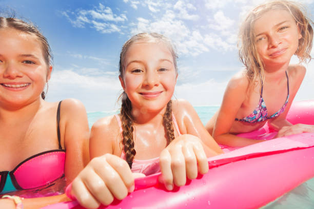 Three girls portrait on the beach matrass Close portrait of three girls swim on the pink matrass in the sea in swimming suits happy and smiling matrass stock pictures, royalty-free photos & images