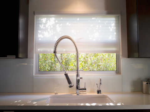White kitchen sink with white tap with window on the background and flower, bright kitchen design, water consumption
