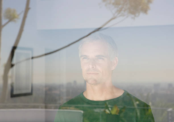 мужчина выглядывает из окна гостиной - window reflection стоковые фото и изображения