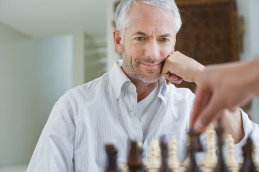 Old man sitting at home and playing chess by itself.
