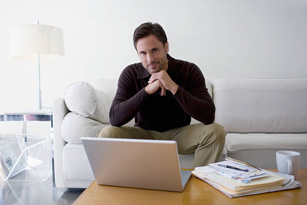 homme assis sur un canapé avec des documents et ordinateur portable - connection usa coffee cup mug photos et images de collection