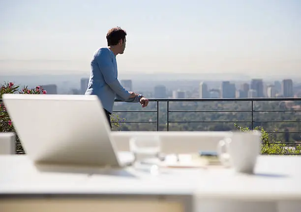 Photo of Man using laptop on balcony overlooking city
