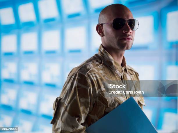 Man In Camouflage Holding Folder Near Bank Of Computers Stock Photo - Download Image Now