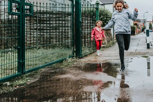 Stock photo of 2 sisters jumping in puddles. File has a signed model released.