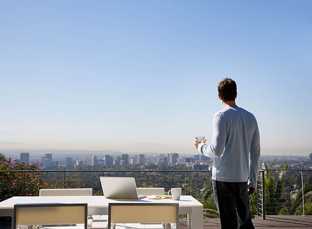 mann mit laptop auf balkon mit blick auf die stadt - balkon stock-fotos und bilder