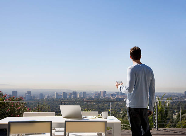 man using laptop on balcony overlooking city - 露台 人造空間 個照片及圖片檔