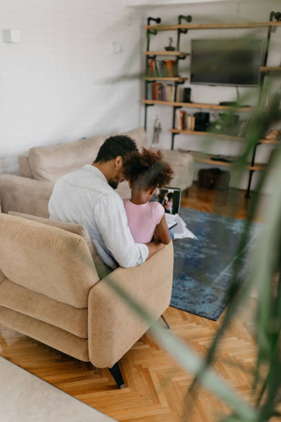 istock Rear view at embraced father and daughter sitting on a sofa 886230294