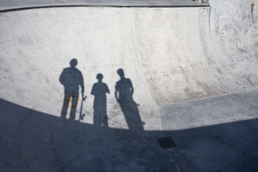 Three silhouetted males in a concrete outdoor skate park.
