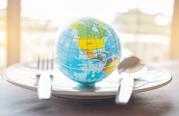 Globe model placed on plate with fork, menu in famous hotels. International cuisine is cuisine that is practiced around the world, often associated with specific region country.