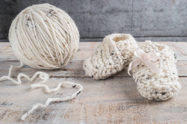 knitting baby booties with bege yarn on wooden table - sewing foot imagens e fotografias de stock