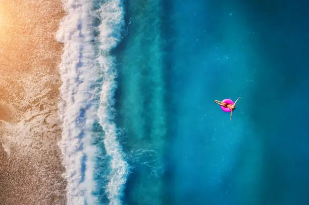 Photo of Aerial view of young woman swimming on the pink swim ring in the transparent turquoise sea in Oludeniz. Summer seascape with girl, beach, beautiful waves, blue water at sunset. Top view from drone