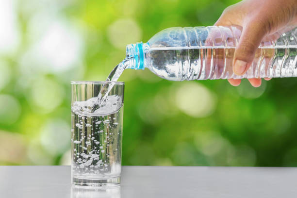 istock hand pouring drinking water into glass form bottle on table with green blur background 886335882