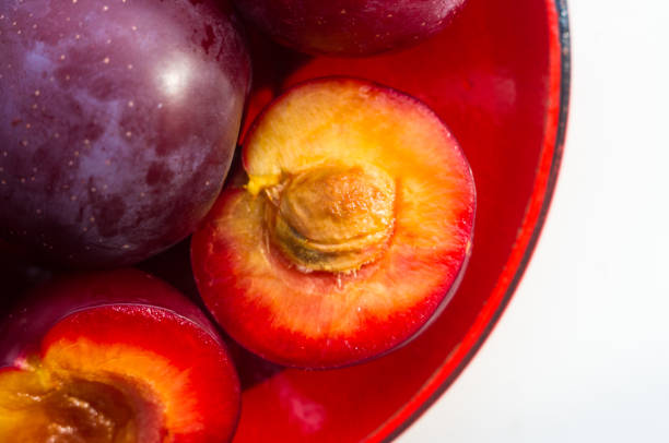 fresh plum fruit with cut plum slices in the red saucer on white background
