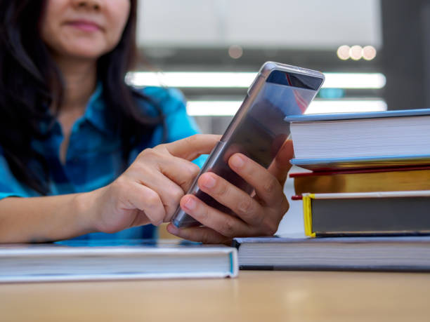 Businesswoman (student) studying, using mobile with stack of books in library stock photo