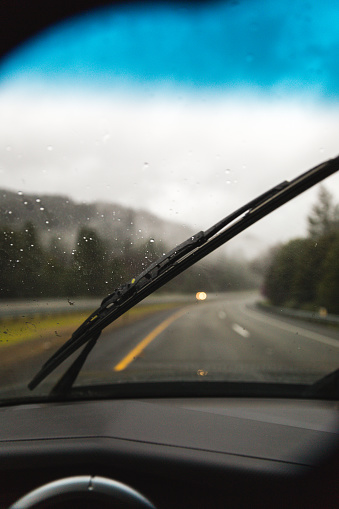 Driver perspective with windshield wiper clearing rain. Forest highway landscape in background.