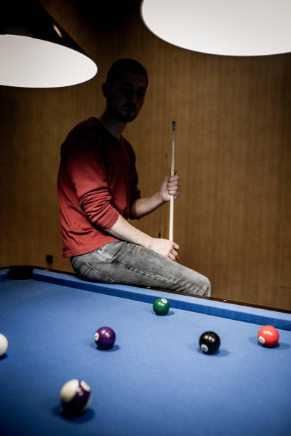 istock Pensive man sitting on a pool table in a hall. 886387792