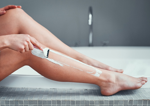 Closeup shot of an unrecognizable woman shaving her legs in the bathroom at home