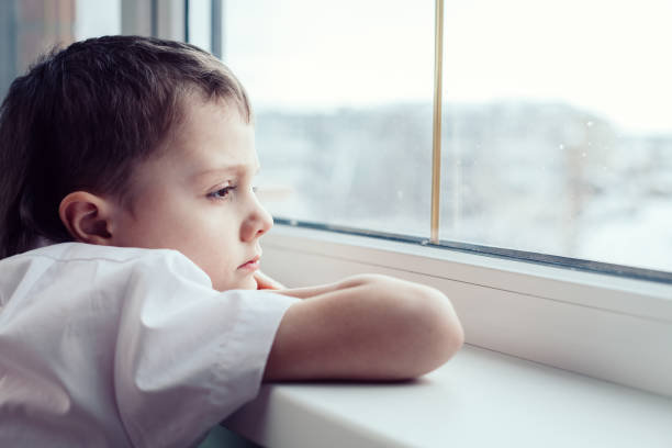 istock sad little boy sitting near the window 886423602