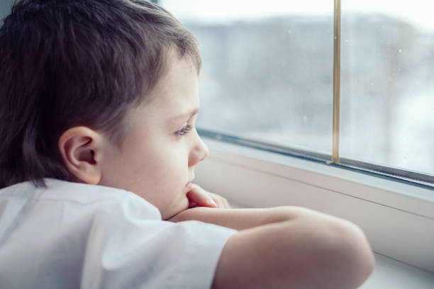 istock sad little boy sitting near the window 886423662