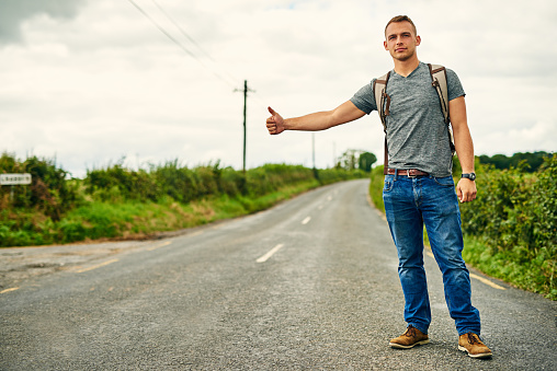 Shot of a young man hitchhiking on the roadside